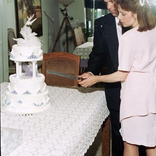 Couple cutting a multi-tiered wedding cake indoors.