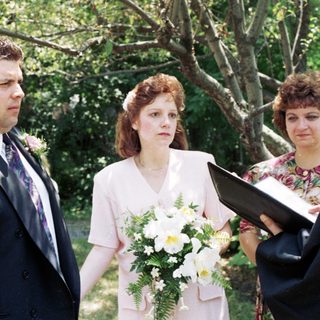 Wedding ceremony with bride, groom, officiant, and guests outdoors.