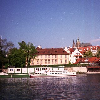 Historic European riverside town with boats and red-roofed buildings.