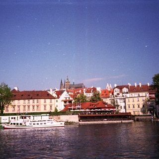 Historic European riverside town with boats and red-roofed buildings.