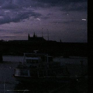 Dramatic evening skyline by river with boats.