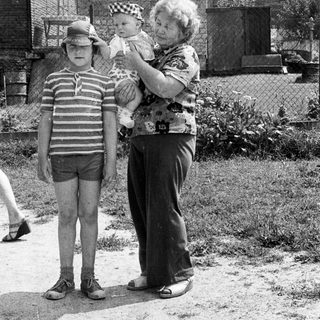 Family moment: elderly woman holding baby, boy standing beside them.