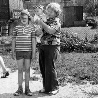Family moment: elderly woman holding baby, boy standing beside them.