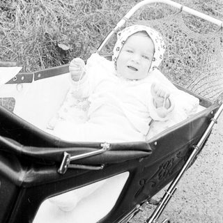 Baby in vintage pram outdoors, smiling.