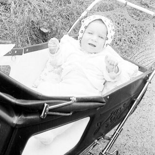 Baby in vintage pram outdoors, smiling.