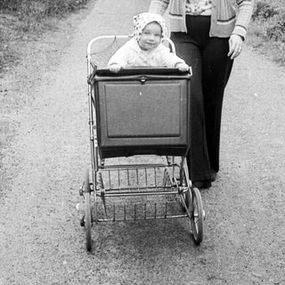 A woman pushes a baby stroller on a rural path.