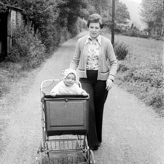 A woman pushes a baby stroller on a rural path.