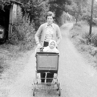Woman pushing stroller with child on rural road.
