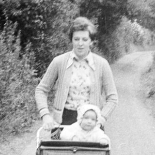 Woman pushing stroller with child on rural road.