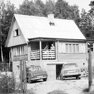 Rural wooden house with two vintage cars parked outside.