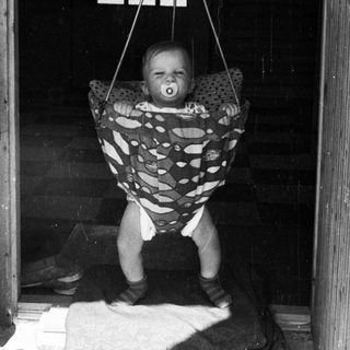 Baby suspended in hanging seat indoors.