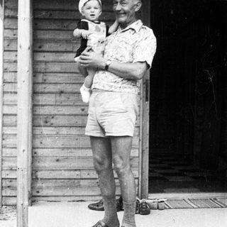 Older man holding young child outdoors.