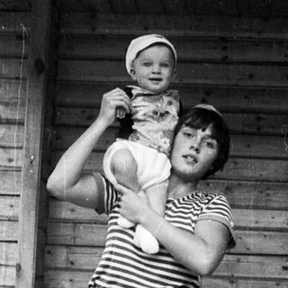 A woman holding a baby outside a wooden shed.