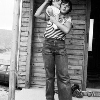 A woman holding a baby outside a wooden shed.