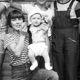 Family posing together outdoors near a rustic building.