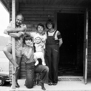 Family posing together outdoors near a rustic building.