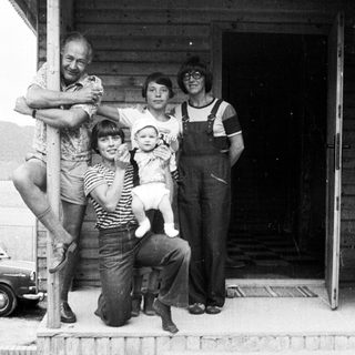 Family posing together outdoors near a rustic building.