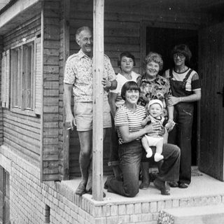 Family posing together outside wooden house porch.