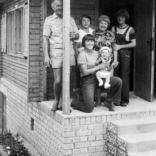 Family posing together outside wooden house porch.