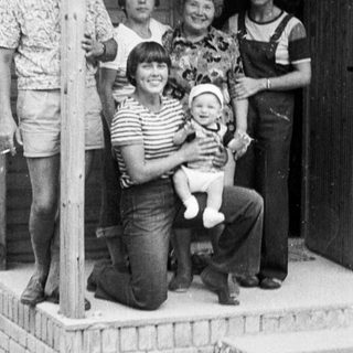 Family posing together outside wooden house porch.