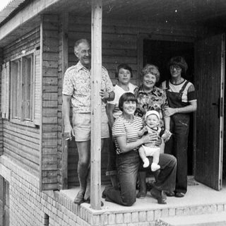 Family posing together outside wooden house porch.