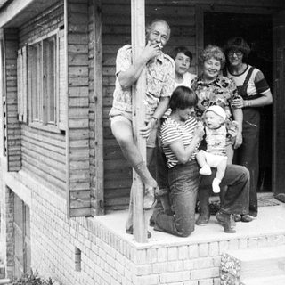 Family group photo outside a wooden house.