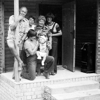 Family group photo outside a wooden house.