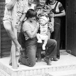 Family group photo outside a wooden house.