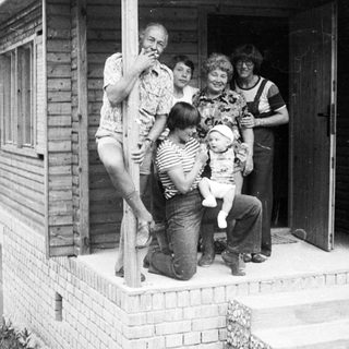 Family group photo outside a wooden house.