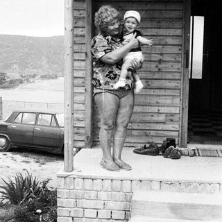 A woman holds a baby on a porch.