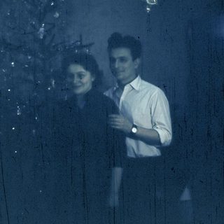 Couple standing indoors near Christmas tree.