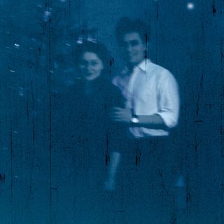 Reflection of two people indoors near window.