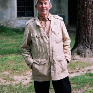 Man in vintage military jacket posing near historic tower.
