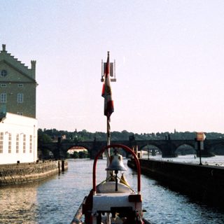 Scenic river view with boat, historic building, bridge.