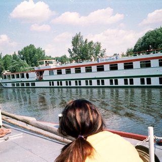 Boat on river with cruise ships in background.