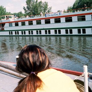 Boat on river with cruise ships in background.