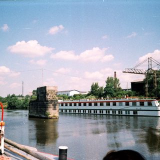 Industrial river scene with boat, bridge ruins, and factory.