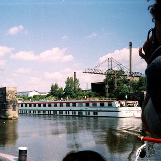 Industrial river scene with boat, bridge ruins, and factory.