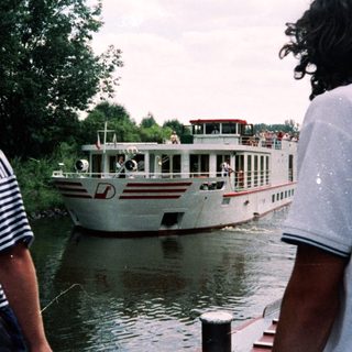 Two men by river watching cruise boat.