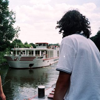 Two men by river watching cruise boat.