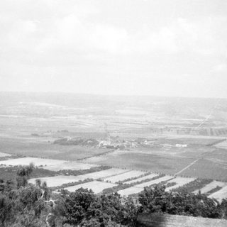 Rural landscape with plowed fields and distant structures.
