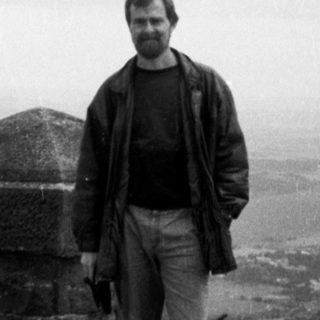 Man standing on elevated stone terrace overlooking city.