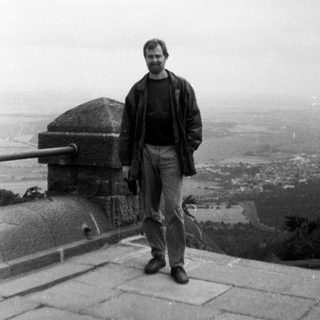 Man standing on elevated stone terrace overlooking city.