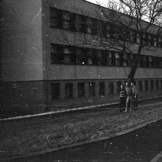 Two people walking alone at night near a building.