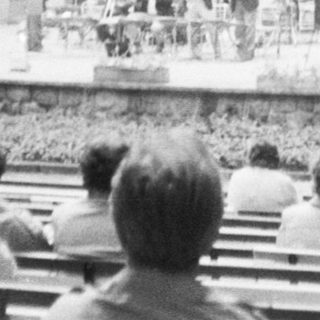 Outdoor stage performance with seated audience in park setting.