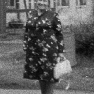 Vintage photo of woman walking past "Kavarna" café building.