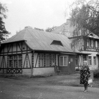 Vintage photo of woman walking past "Kavarna" café building.