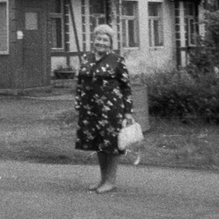 Vintage photo of woman walking past "Kavarna" café building.