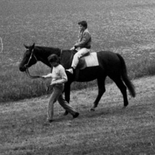 Two riders on horseback near a lake.