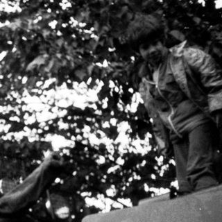 Armored vehicle with soldier in forested combat scene.